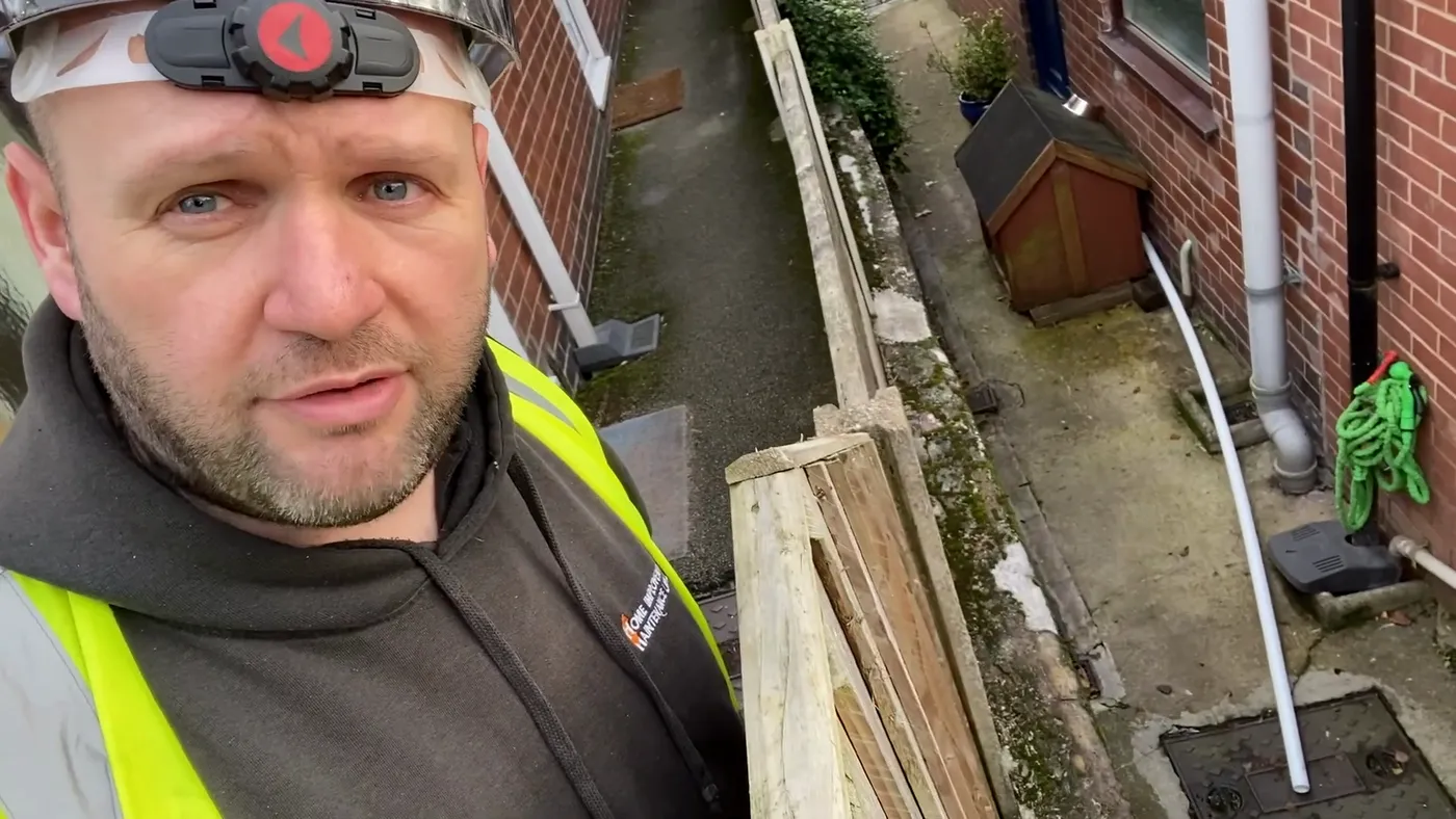 The narrow passage down the side of a house, with a downpipe running to a gully at ground level.