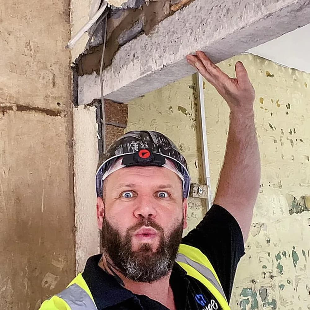 John standing beneath a newly installed concrete lintel spanning a new opening, hand raised against it.