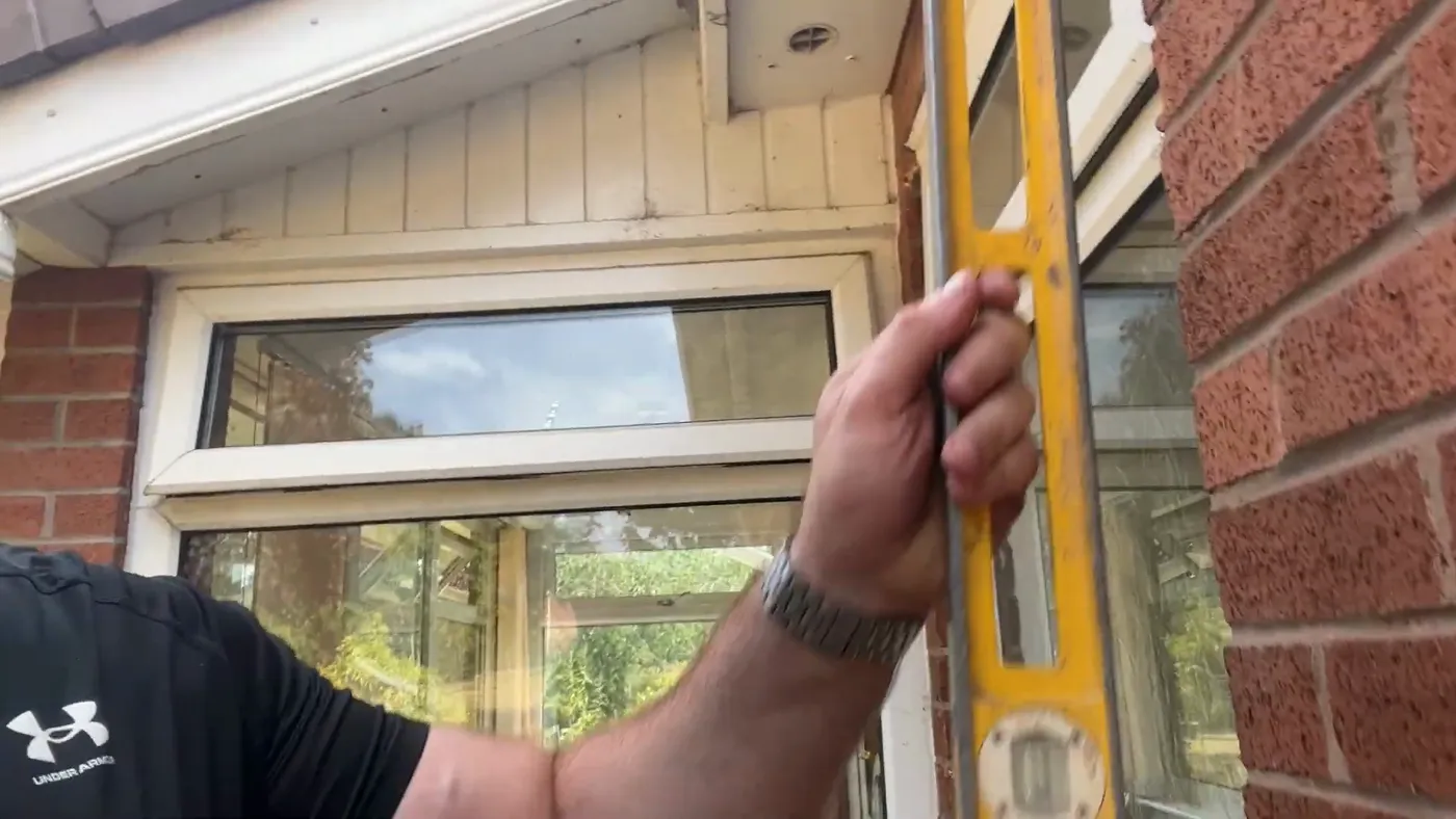 A spirit level held vertically against a window reveal to check whether it is plumb.