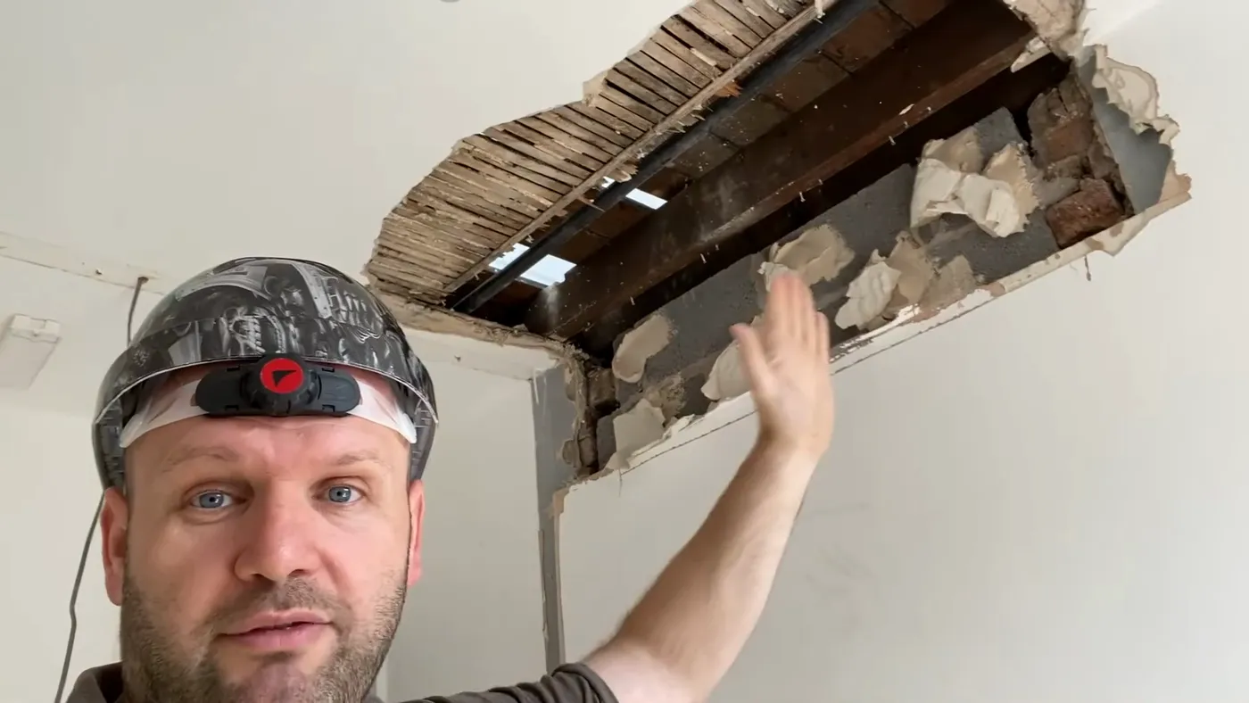 John pointing up into a ceiling opened up to expose damaged joists and rubble in a poorly converted HMO.