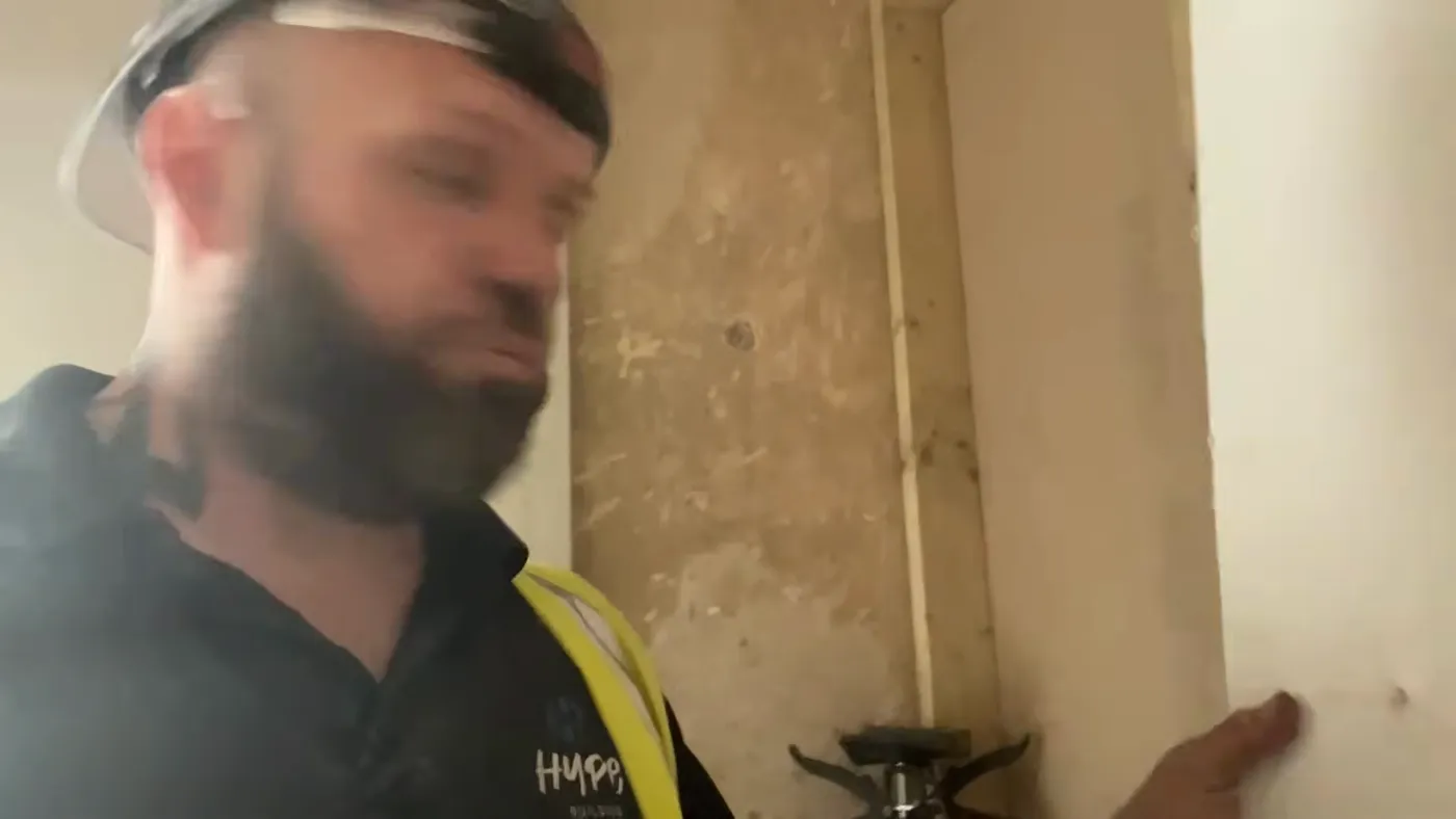 A fitted insulated plasterboard sheet sitting flush against the wall, with John pointing to the finished edge.