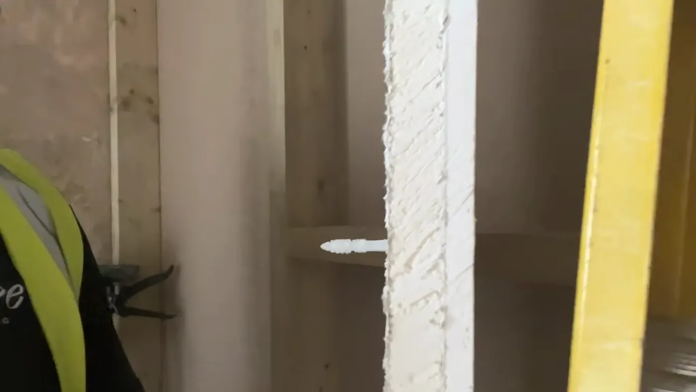 An insulation fixing driven through an insulated plasterboard sheet into the wall behind, beside a bead of panel adhesive.
