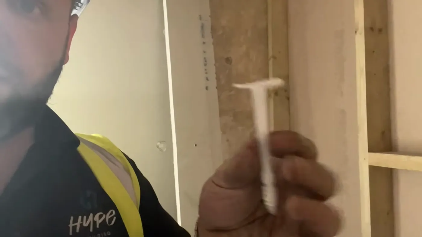 A white plastic insulation fixing held in the hand, with a wide flat head and a ribbed shank.