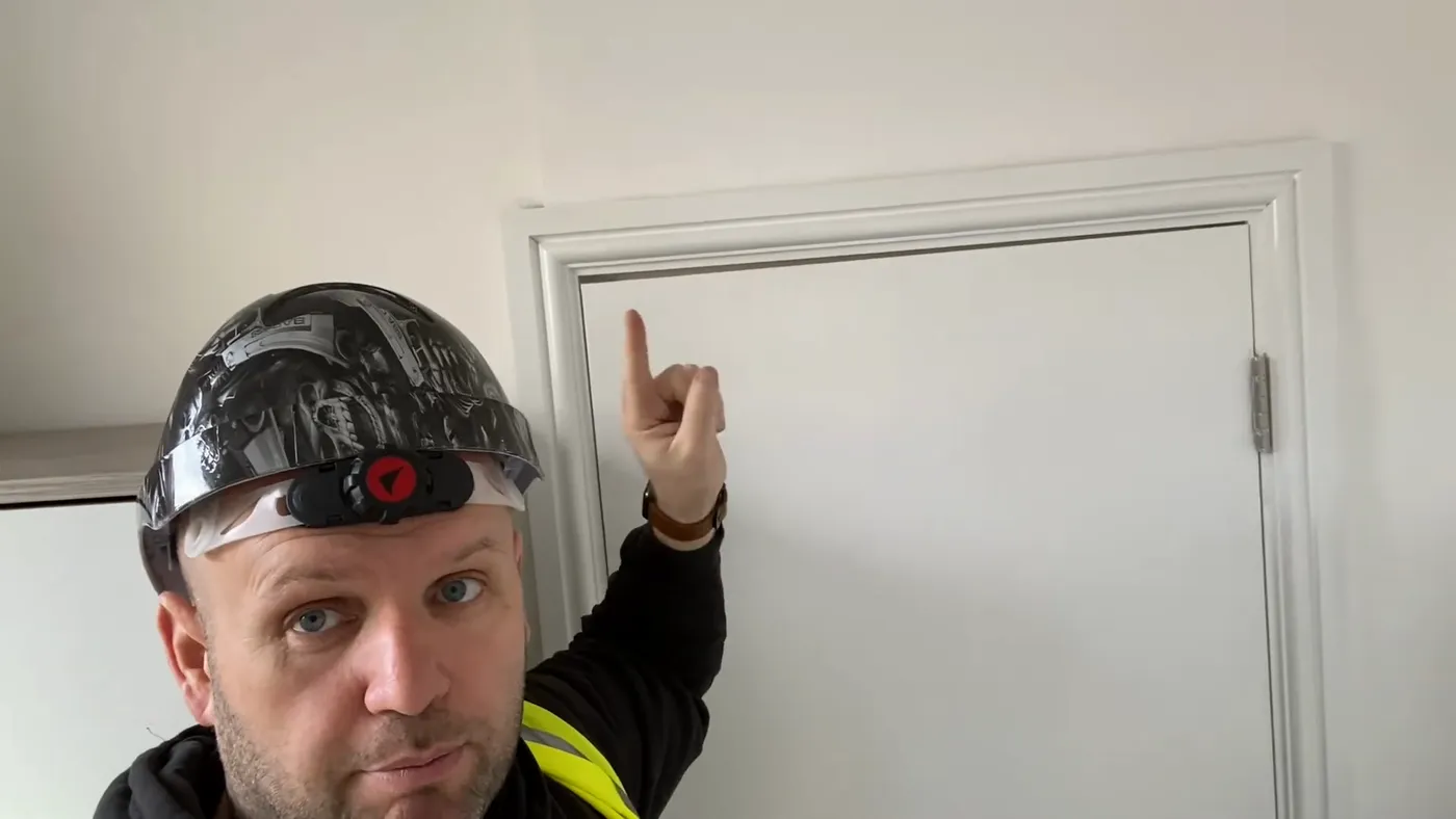 John pointing at a plain flush door in a refurbished HMO that has no intumescent strip or door closer fitted.