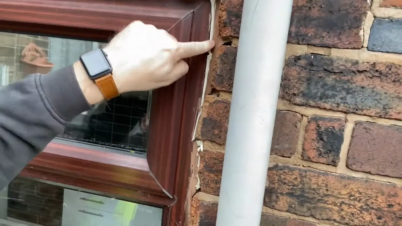 A thick, badly applied bead of sealant smeared where a downpipe meets a window reveal and brickwork.