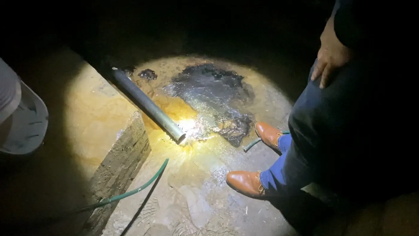 A wet cellar floor lit by torchlight, with a pipe running across it and standing water pooling.