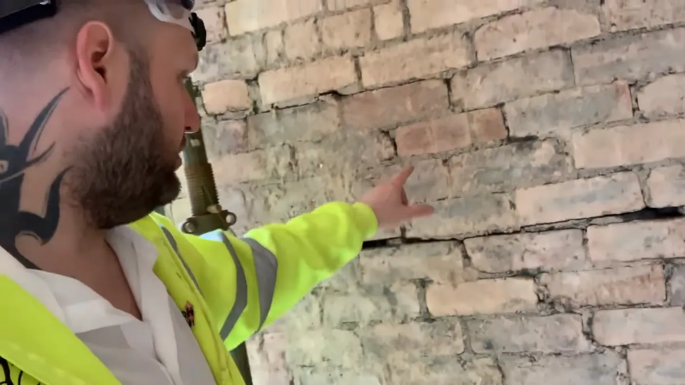 John pointing at a long horizontal crack running along a mortar bed joint in an external brick wall.