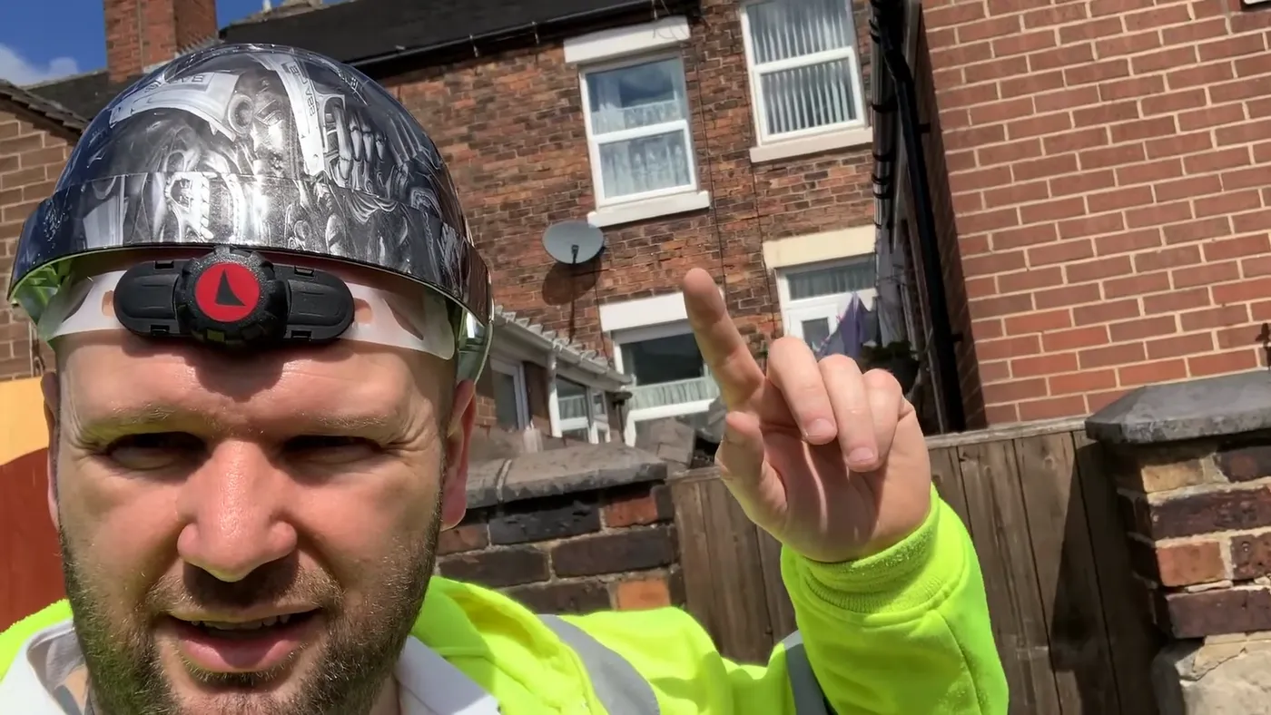 John standing outside the rear of the affected terraced property, pointing up towards the elevation, with the adjoining house alongside.