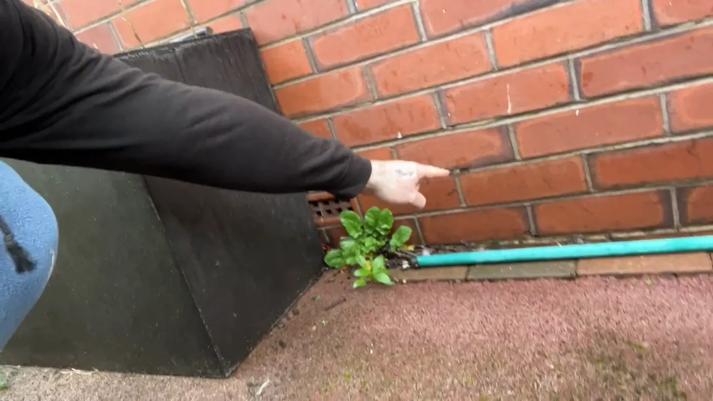 A hand pointing at a clay air brick set into external brickwork just above ground level.